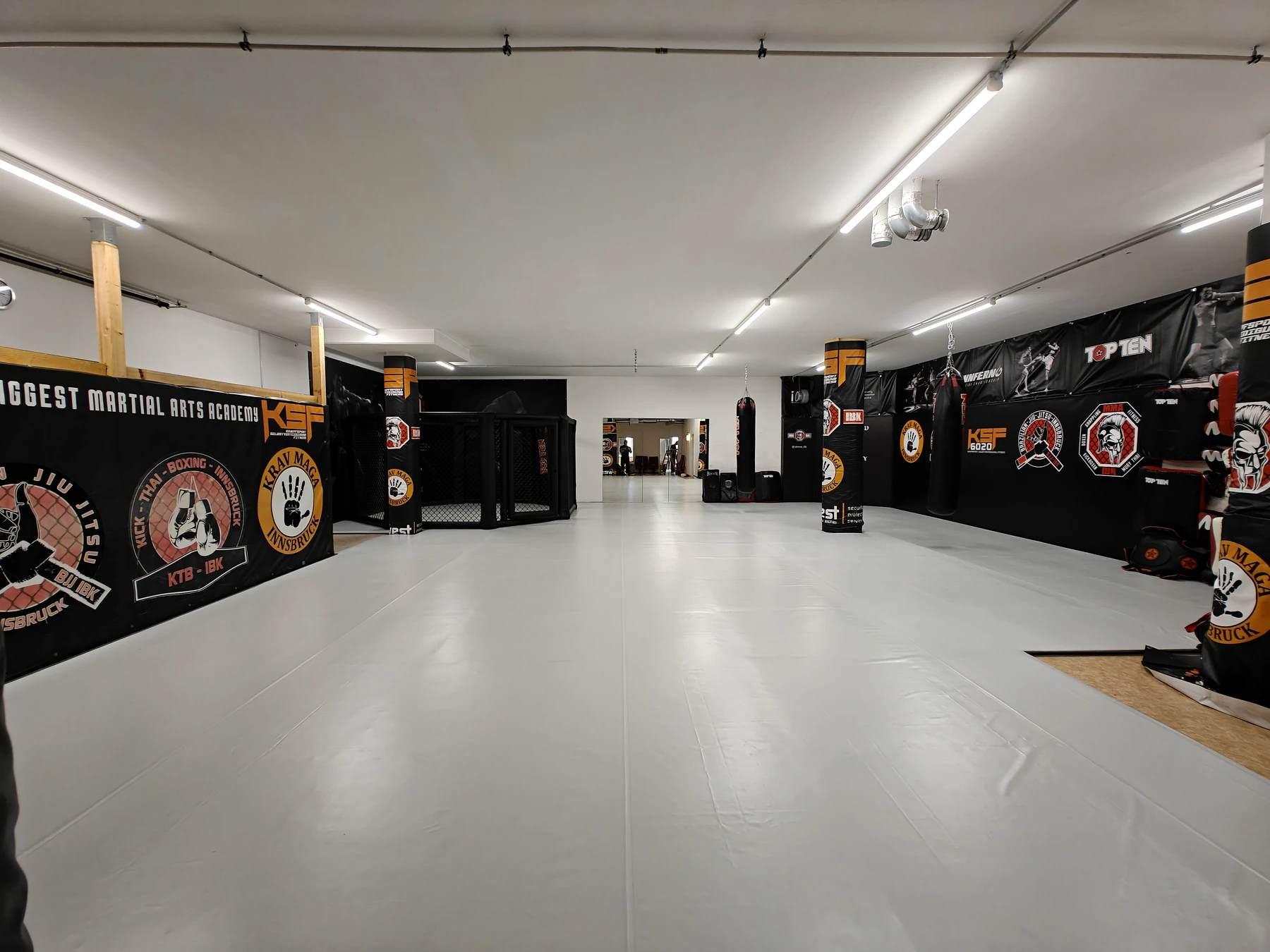 Große helle Trainingshalle mit Cage und Wandbannern